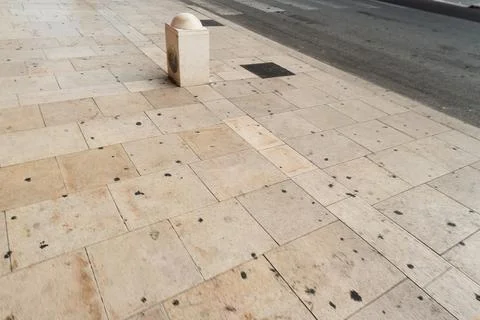 Limestone paved sidewalk with a single stone bollard and a drain grate beside an Stock Photos