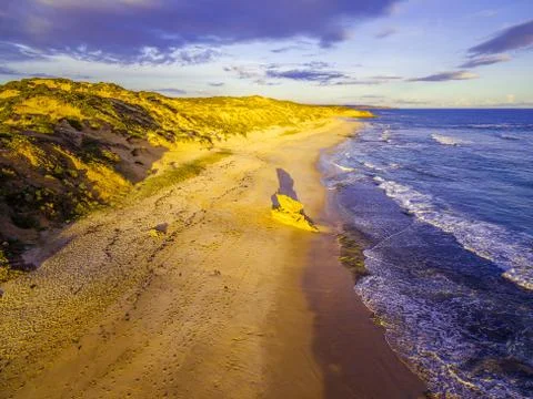 Limestone rock formation with long shadow on ocean beach glowing at sunset Stock Photos