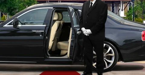 Limo driver standing next to opened car door with red carpet Stock Photos