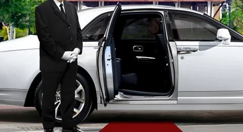 Limo driver standing next to opened car door with red carpet Stock Photos