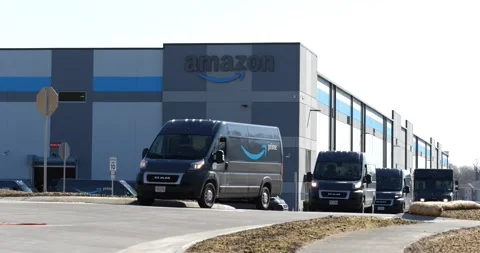 A line of Amazon vans pull out of an Amazon warehouse Stock Footage 151669837