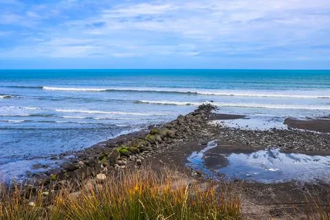 A line of black rocks points out to sea under a cloudy sky Stock Photos