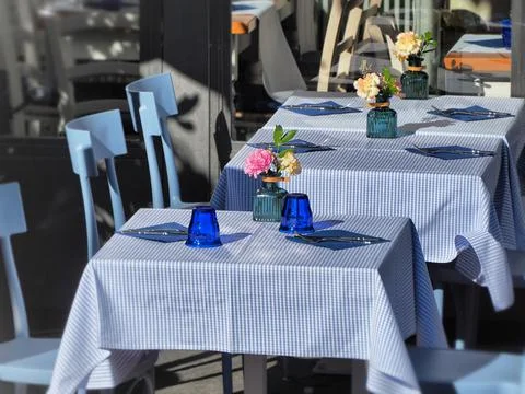 A line of cute square tables with patterned blue and white tablecloths and fl Stock Photos