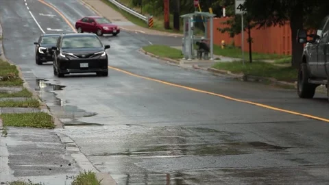Line of dark vehicles coming down wet bridge road and driving over large puddle Stock Footage 247753257