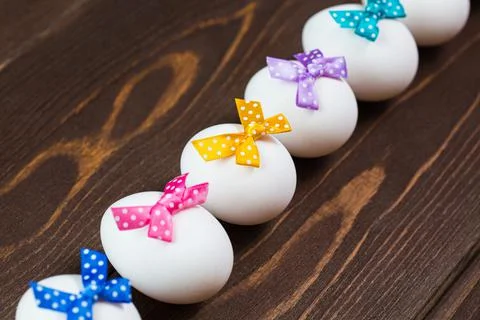Line of easter eggs with colorful bows are on the wooden background. Stock Photos