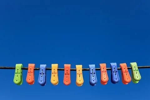 Line of multicolor plastic clothes pegs hanging in front blue sky Stock-Fotos