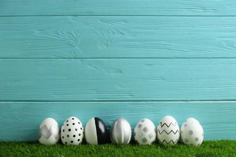 Line of painted Easter eggs on green lawn against wooden background, space fo Stock Photos