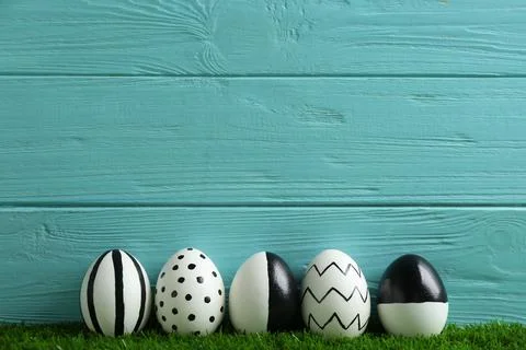 Line of painted Easter eggs on green lawn against wooden background, space fo Stock Photos
