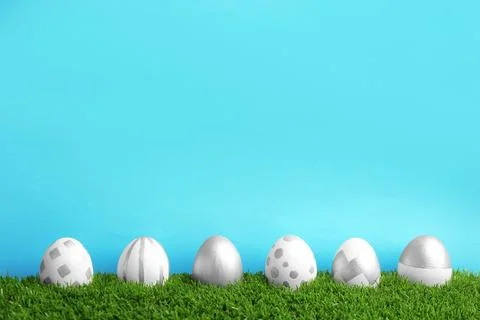 Line of painted Easter eggs on green lawn against color background, space for Stock Photos