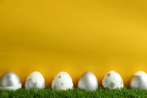 Line of painted Easter eggs on green lawn against color background, space for Stock Photos