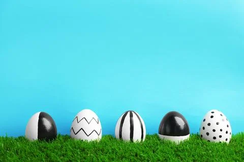 Line of painted Easter eggs on green lawn against color background, space for Stock Photos
