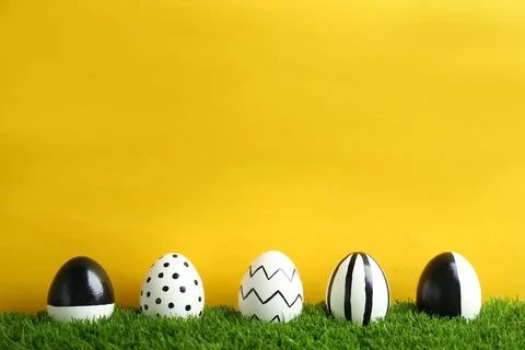 Line of painted Easter eggs on green lawn against color background, space for Foto stock