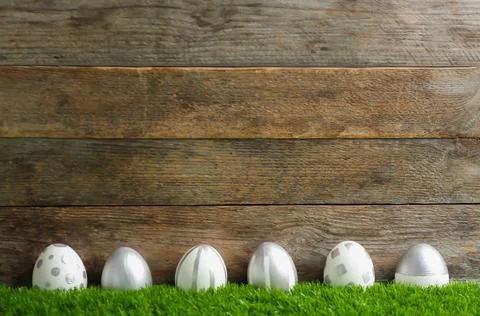 Line of painted Easter eggs on green lawn against wooden background, space fo Stock Photos