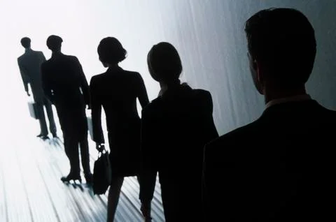 A line of people, men and women in silhouette, walking towards a very bright Stock Photos