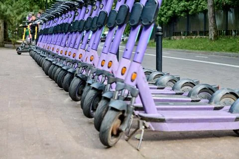 Line of purple e-scooters on sidewalk beside road Stock Photos