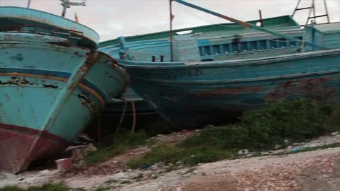 Line row of small wrecked boats ships shipwreck on shore leaning against other Stock Footage 252153442