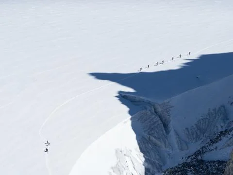 A line of walkers look tiny in contrast to a large glacier which they walk on Stock Photos