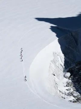A line of walkers look tiny in contrast to a large glacier which they walk on Stock Photos