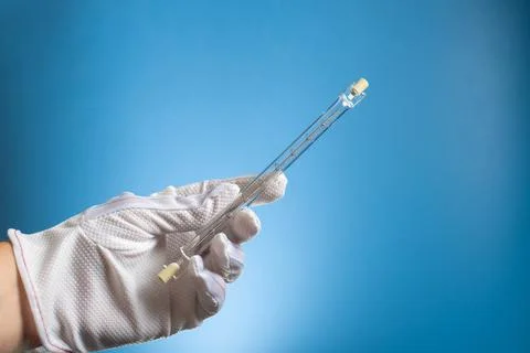Linear halogen lamp with double base R7S. A gloved hand holds a lamp on a blu Stock Photos