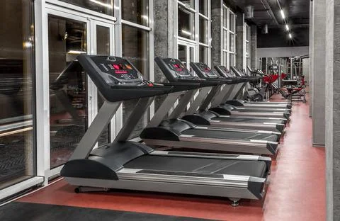 Lined modern treadmills by the window in spacious, well lit, empty gym interior Stock Photos
