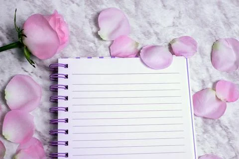 Lined notebook with flowers around it on marble table. Stock Photos