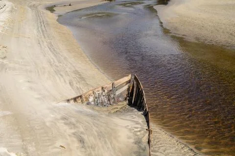 Lines and patterns curving along edge of stream interupted by bow of old wood Stock Photos