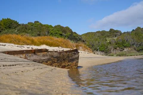 Lines and patterns curving along edge of stream interupted by bow of old wood Stock Photos