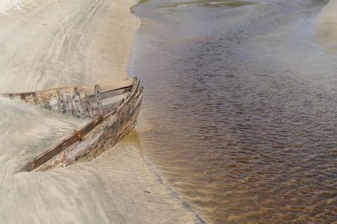 Lines and patterns curving along edge of stream interupted by bow of old wood Stock Photos