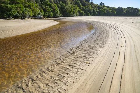 Lines and patterns curving along edge of stream interupted by bow of old wood Stock Photos