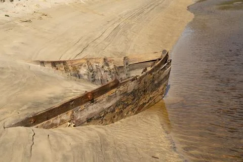Lines and patterns curving along edge of stream interupted by bow of old wood Stock Photos