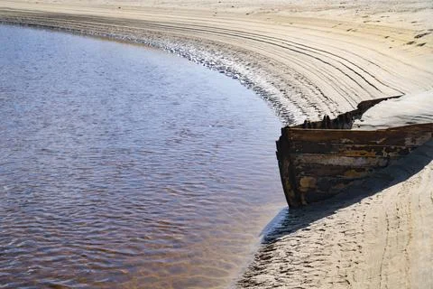 Lines and patterns curving along edge of stream interupted by bow of old wood Stock Photos