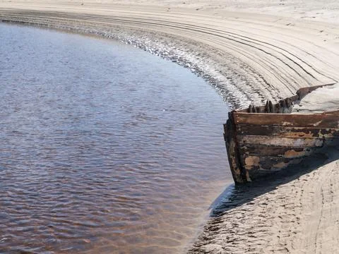 Lines and patterns curving along edge of stream interrupted by bow of old w.. Stock Photos