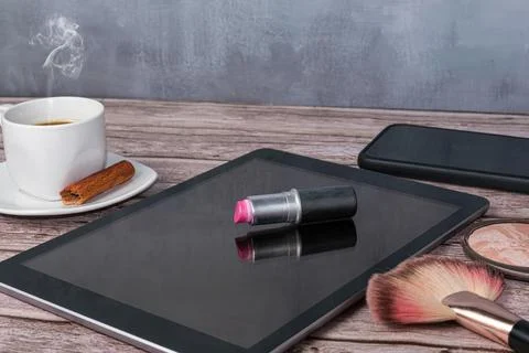 Lipstick on tablet surrounded by coffee cup, smartphone, pressing powder, and Stock Photos