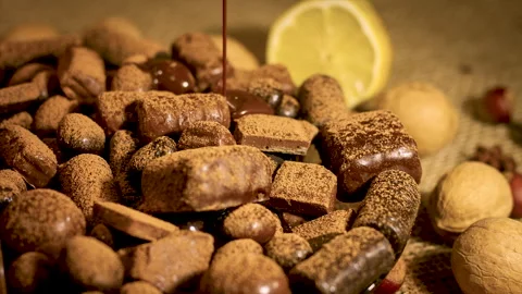 Liquid chocolate flows on assortment of chocolates nuts and citrus fruits Stock Footage 131623800
