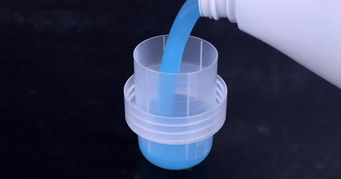 Liquid detergent flowing from the bottle into the container on black Stock Footage 297887027