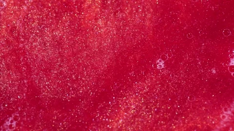 Liquid with dissolved particles of red candurin and bubbles slowly moves and shi Stock Footage 306073857