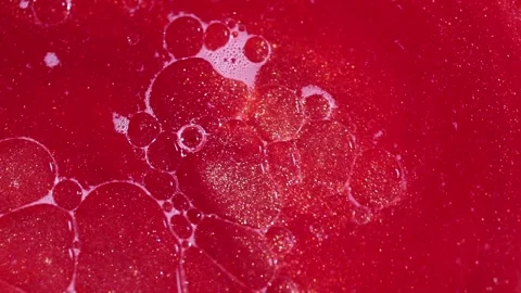 Liquid with dissolved particles of red candurin and bubbles slowly moves and shi Stock Footage 306073963