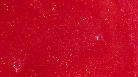 Liquid with dissolved particles of red candurin and bubbles slowly moves and shi Stock Footage 306074051