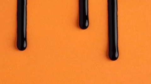 Liquid drops of bright black paint color flowing on the orange surface. Macro Stock Footage 250163417