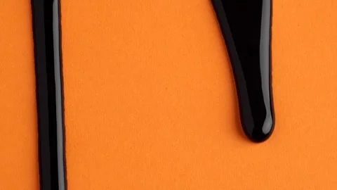Liquid drops of bright black paint color flowing on the orange surface. Mac.. Video stock 251541776
