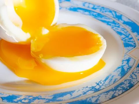 Liquid egg yolk flows onto a plate. Stock Photos