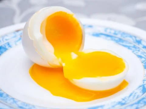 Liquid egg yolk flows onto a plate. Stock Photos