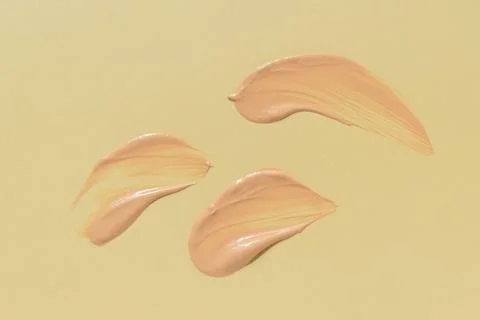 Liquid foundation texture smeared on yellow background, smooth makeup strokes 스톡 사진