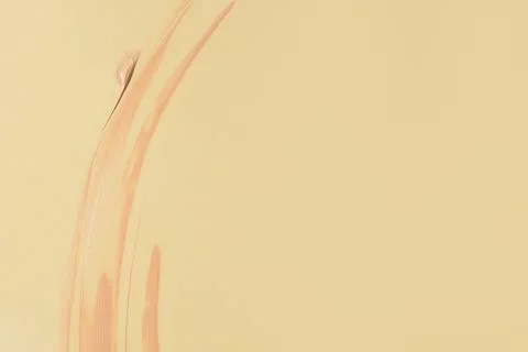 Liquid foundation texture smeared on yellow background, smooth makeup strokes 스톡 사진