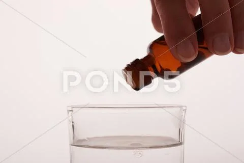 Liquid medication dripping into a glass of water Stock Photos