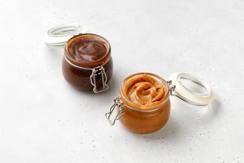 Liquid melted caramel syrup, paste in round glass jars with lid isolated on.. 库存照片