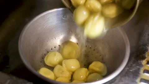 Liquid pours into strainer then dumplings settle within metal bowl Stock Footage 331726319