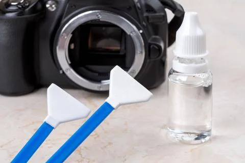 Liquid sensor cleaner and two swabs against dslr camera with lens removed. Stock Photos