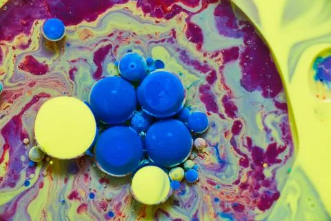 Liquid surface of rainbow colors with floating blue and yellow spheres Фото
