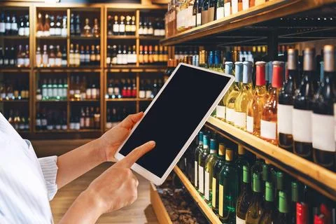 Liquor store manager using digital tablet in front of half of wine bottles. B Stock Photos